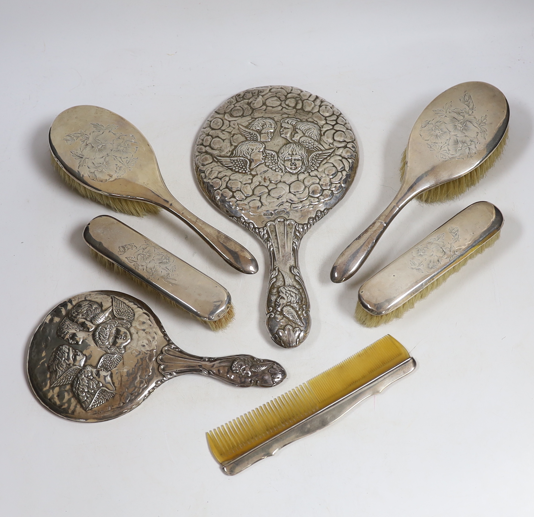 Two early 20th century repousse silver mounted hand mirrors with Reynold's Angels decoration, four silver mounted brushes and a comb.